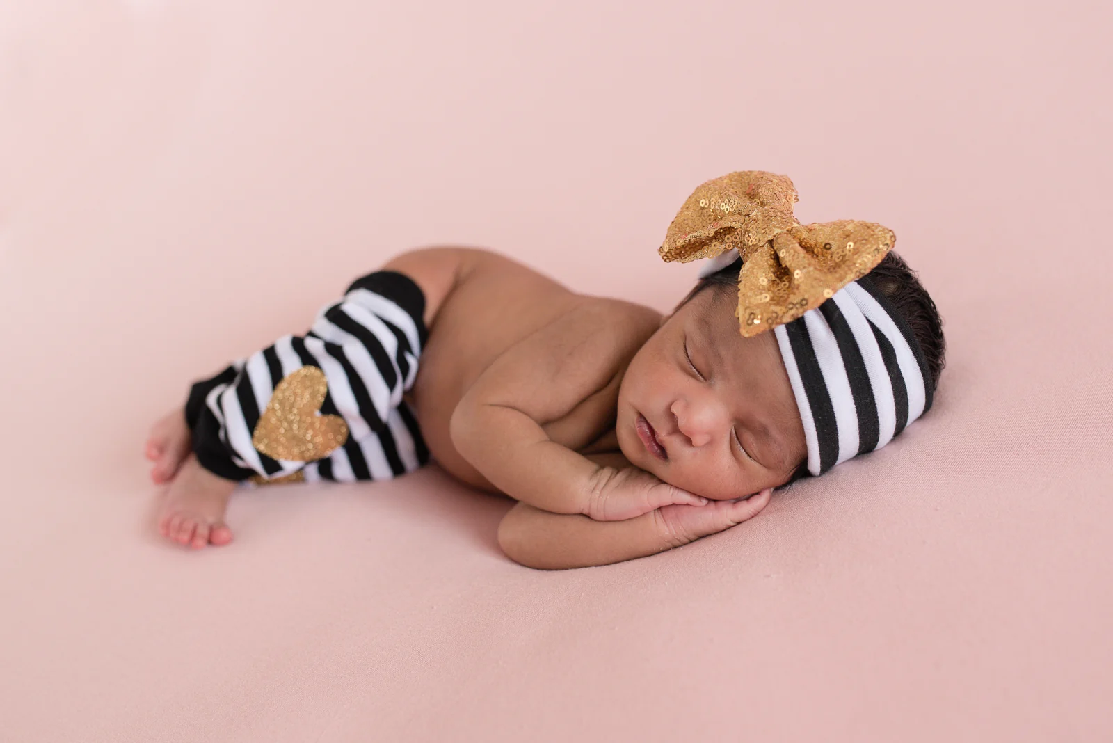 A sleeping newborn with a bow on a soft pink backdrop