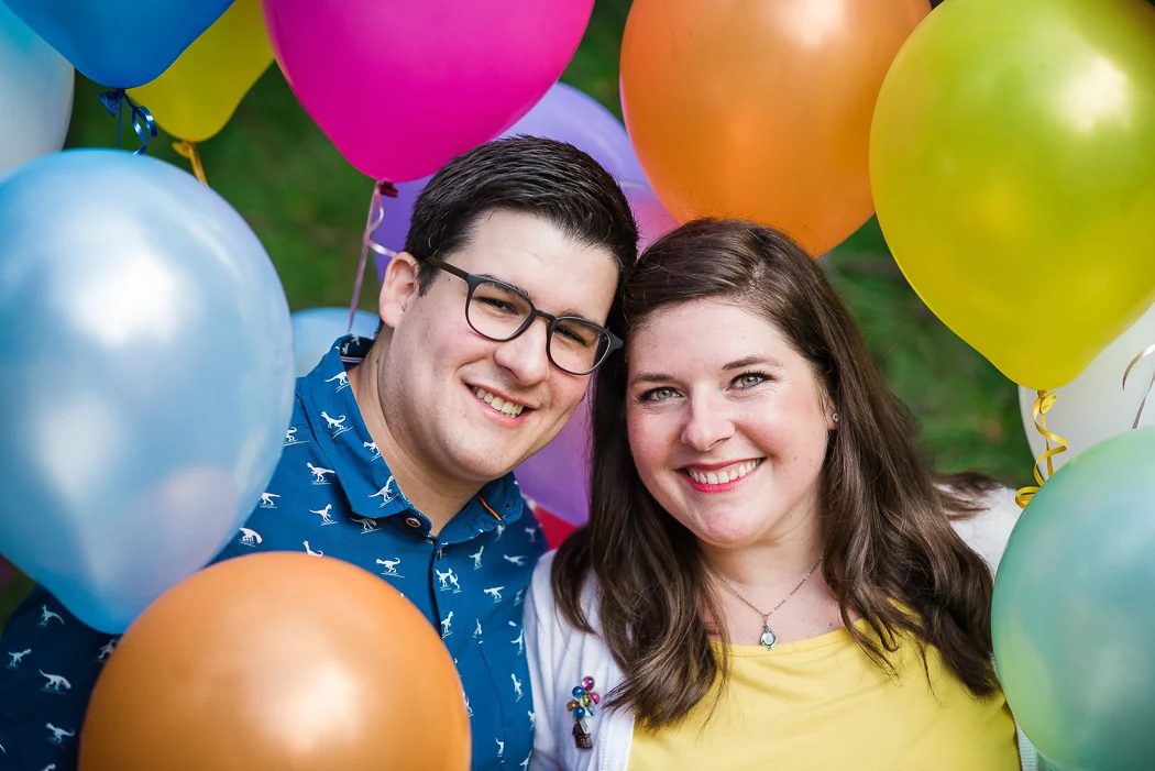 An engaged couple laughing in front of colorful balloons