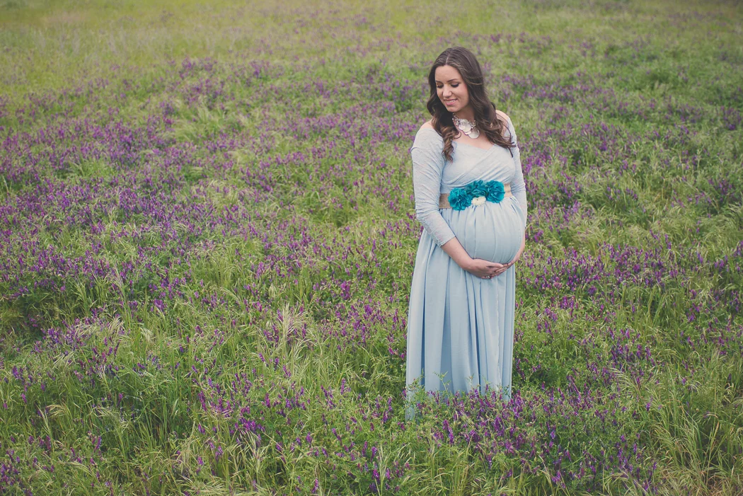 An expectant mother in a pale blue dress among wildflowers